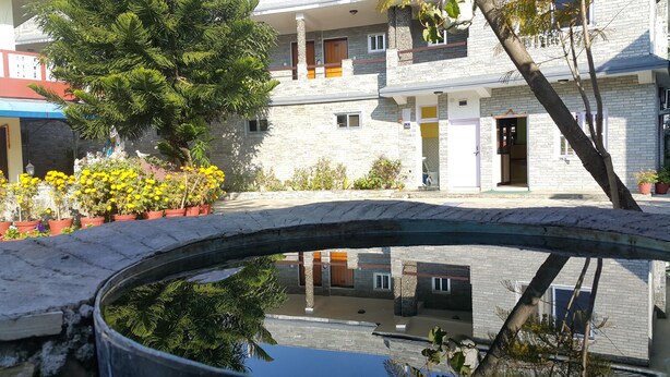 A multi-story building with a stone facade, balconies, and a small bridge over a water feature. - Hotel Bishram (Pokhara)