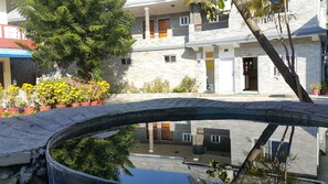 Un edificio de varios pisos con fachada de piedra, balcones y un pequeño puente sobre una fuente de agua.