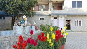 A courtyard with a statue, potted plants, and a building with stone walls and windows. - Hotel Bishram (Pokhara)