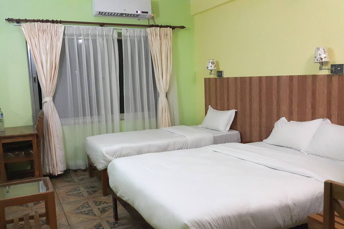 Habitación de hotel con dos camas, cabecera de madera, una mesita, televisor y ventana con cortinas.