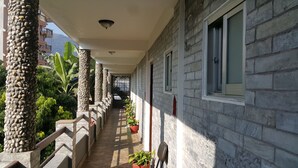 A covered outdoor corridor with stone pillars, potted plants, and a view of a mountainous landscape. - Hotel Bishram (Pokhara)