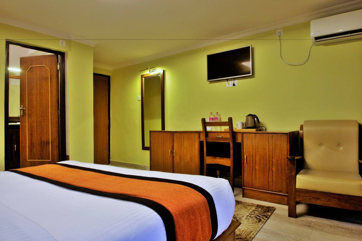 A hotel room with a bed, a wooden wardrobe, a television mounted on the wall, and a chair.