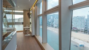 Een moderne hotelkamer met grote ramen, uitzicht op het strand en een stadsbeeld.