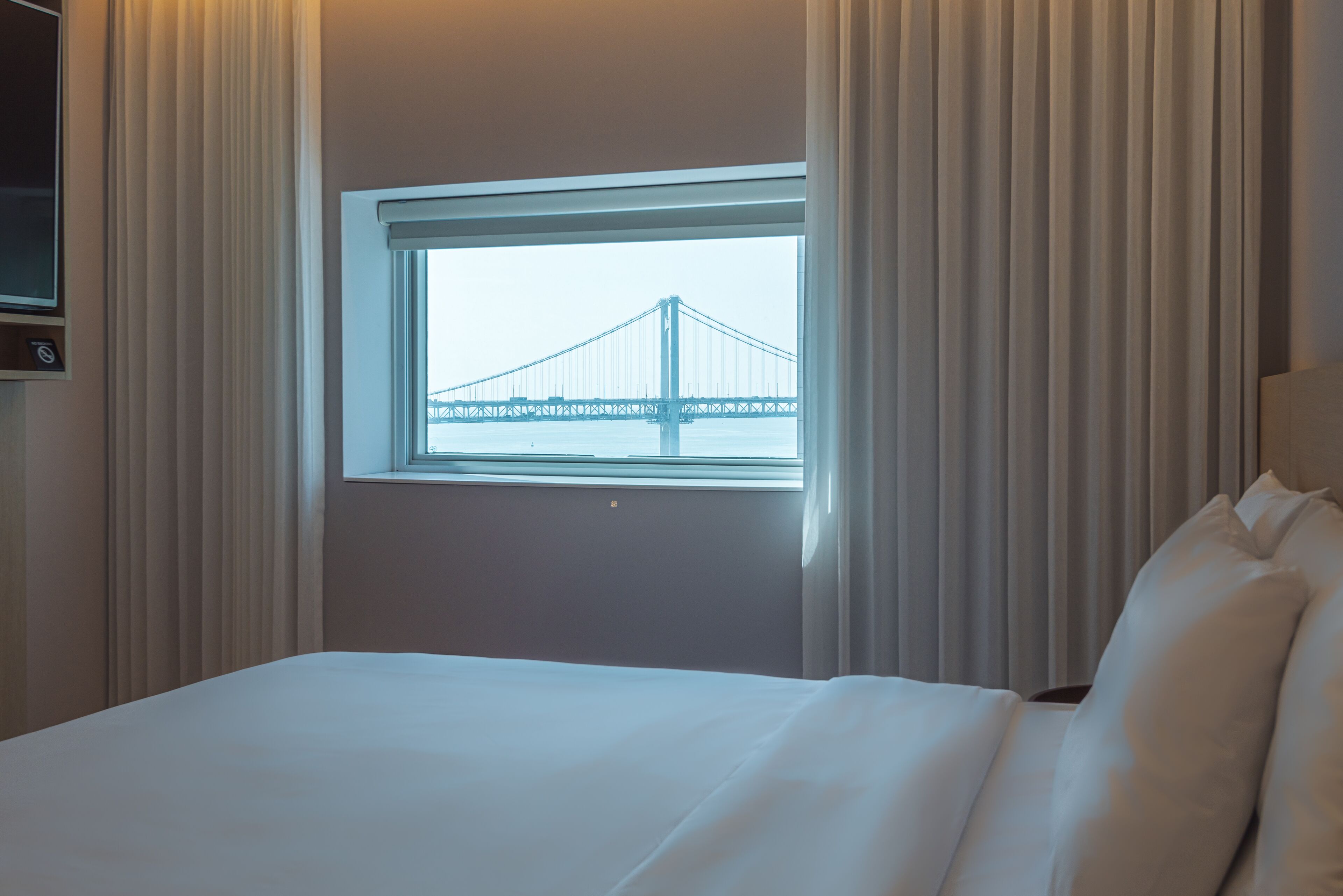 A hotel room with a large bed, a window with a view of a bridge, and curtains.