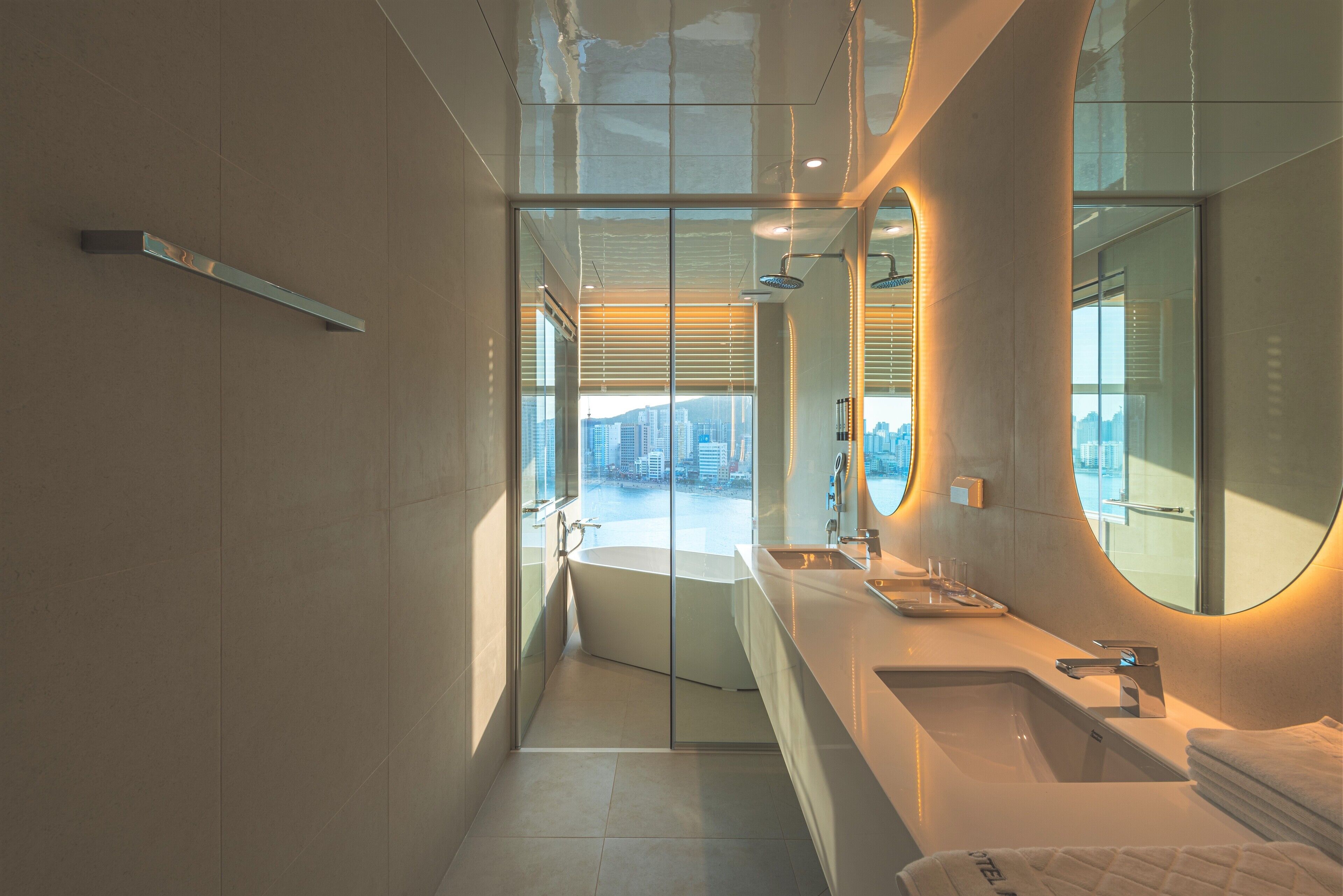 A modern bathroom with a glass-enclosed shower, a large mirror, and a view of the cityscape.