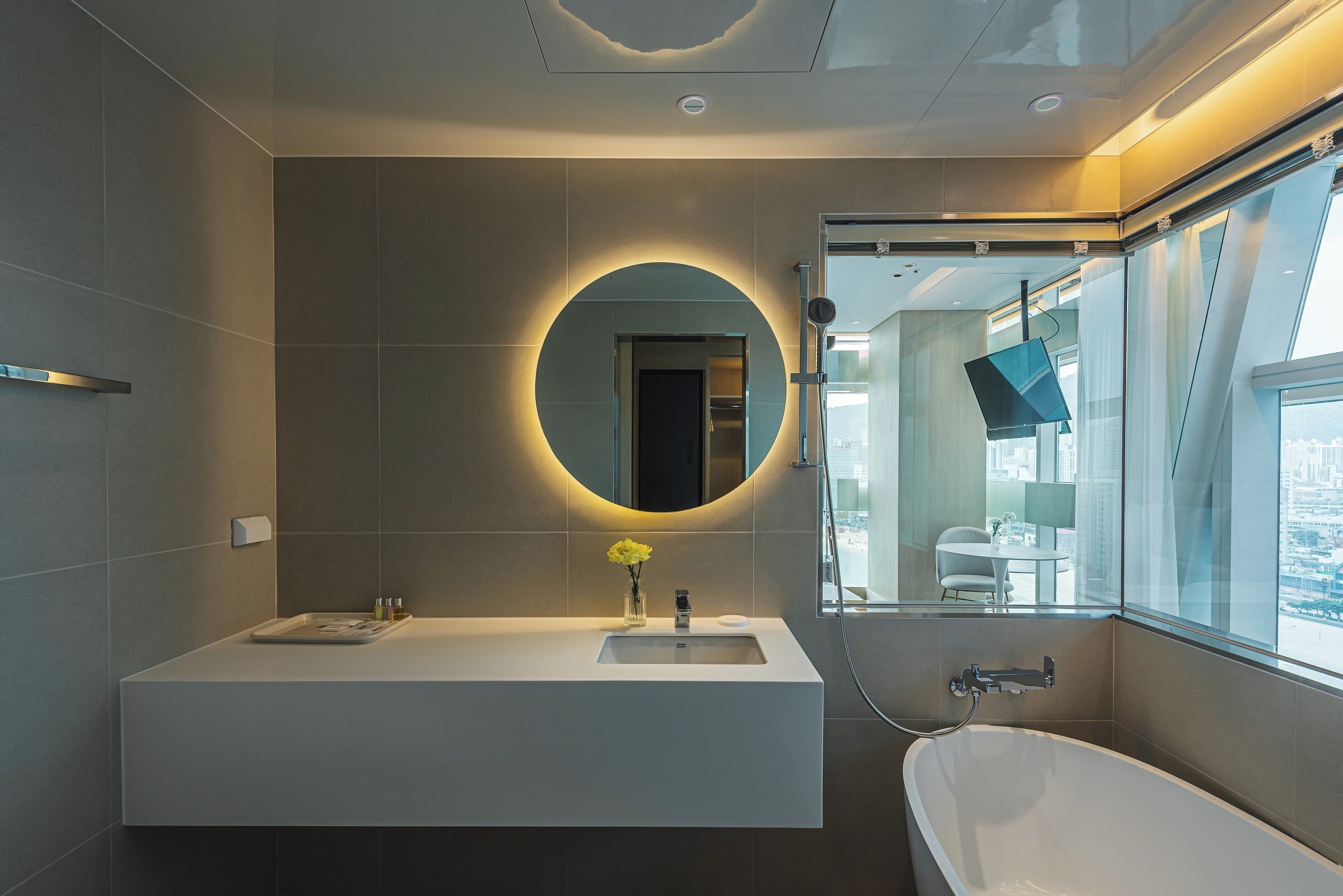 A modern bathroom with a large mirror, a bathtub, and a window with a view of the city.
