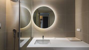 Une salle de bain moderne avec une douche à parois de verre, un grand miroir à cadre rond et un lavabo blanc doté d’un porte-savon.