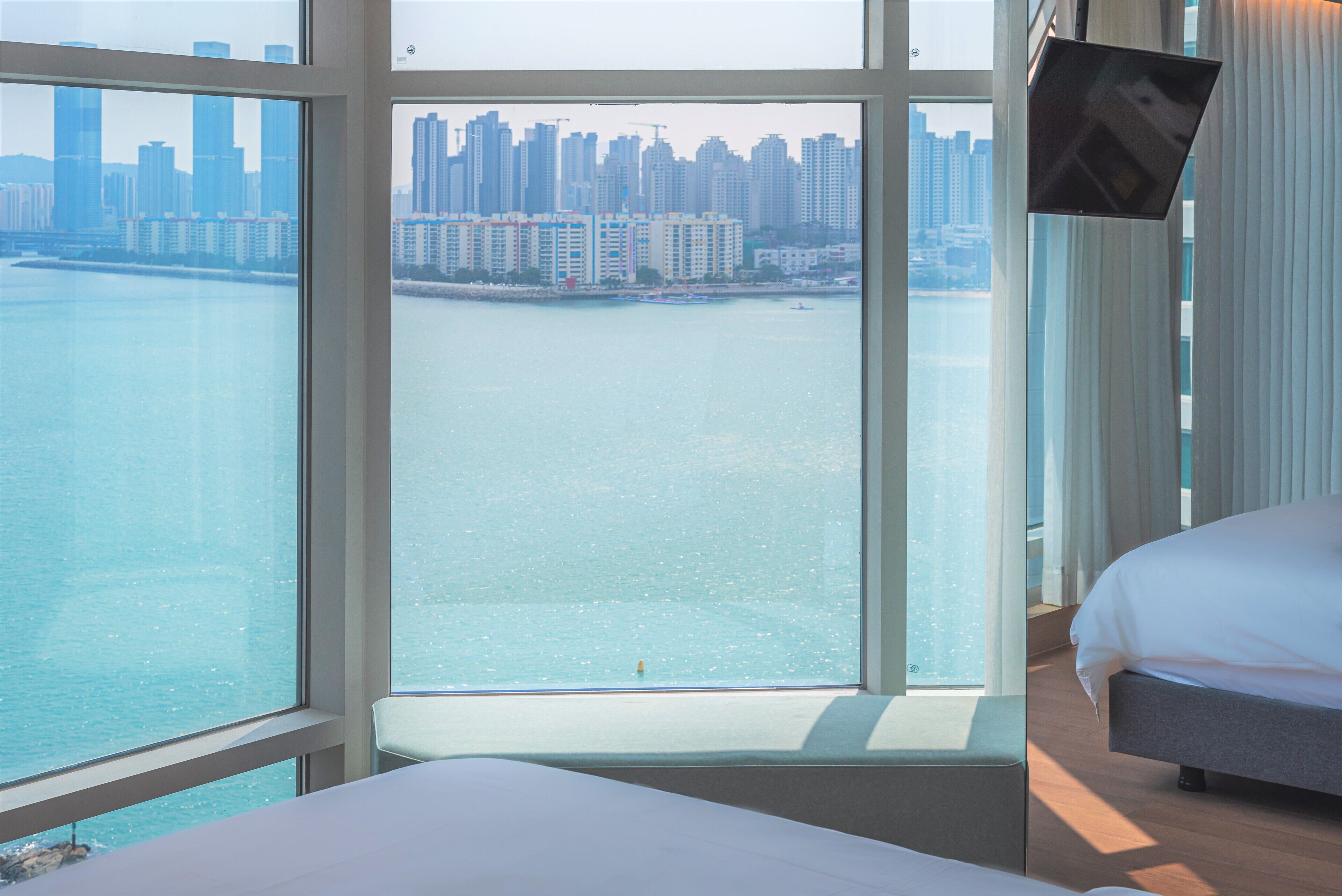 A hotel room with a large window offering a view of a city skyline and water.