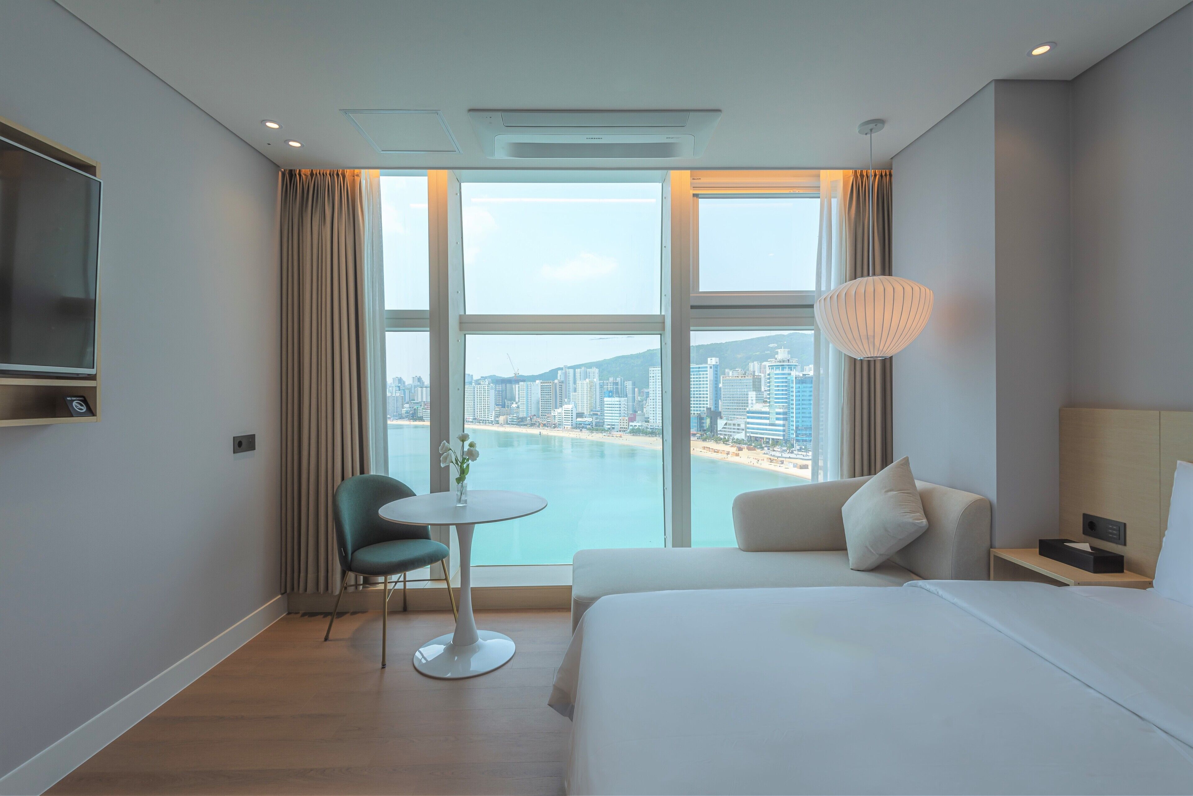 Habitación de hotel con un ventanal grande, una cama, un escritorio, una silla y un televisor.