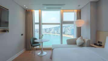 Habitación de hotel con un ventanal grande, una cama, un escritorio, una silla y un televisor.
