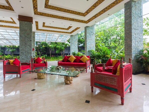 Un vestíbulo espacioso con sofás rojos, una mesa de centro de vidrio y grandes ventanales con vistas a un exuberante jardín.