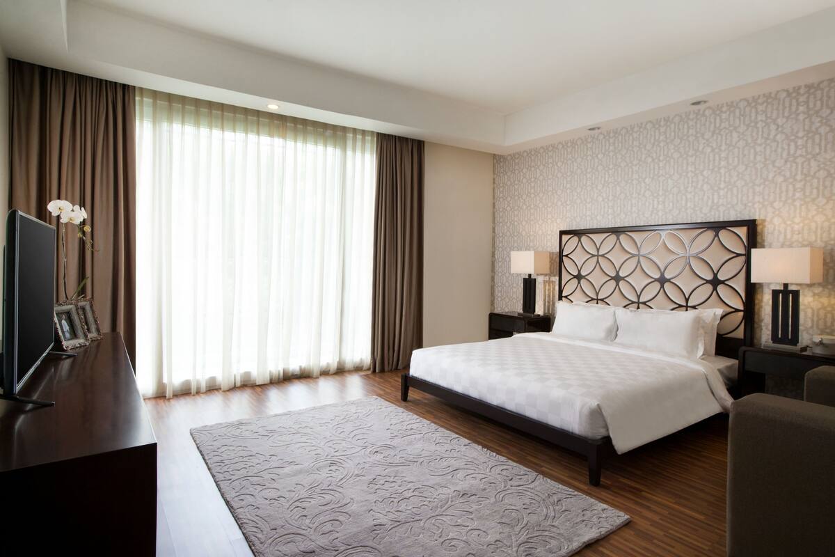 A hotel room with a large bed, two bedside tables with lamps, a television, and a decorative plant.