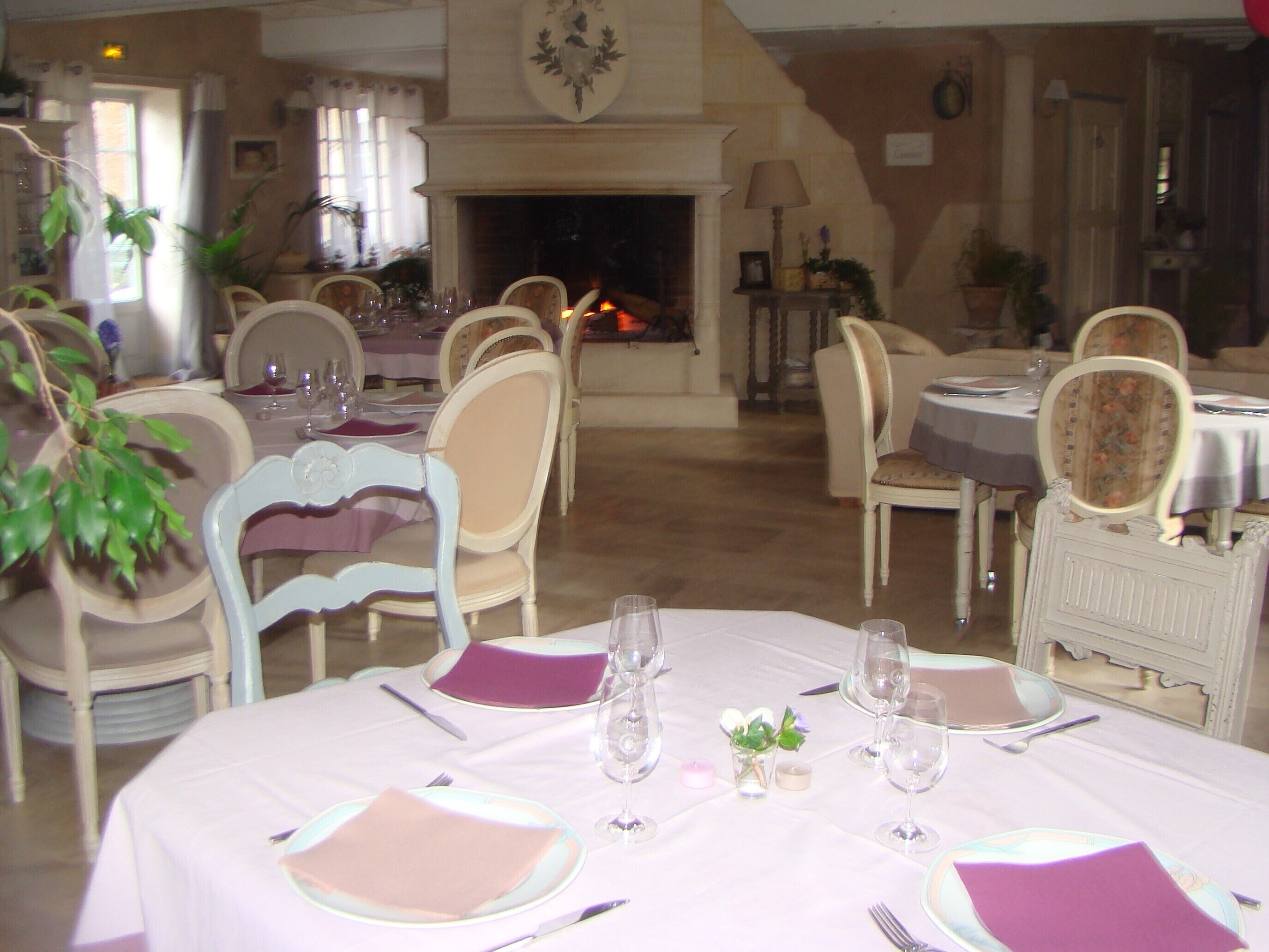Un espace repas avec des tables rondes dressées pour le repas, des chaises et une cheminée en arrière-plan.