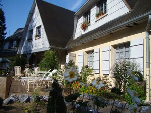 Ein zweigeschossiges Haus mit Garten. Vor dem Haus befindet sich eine Terrasse mit Gartenmöbeln.