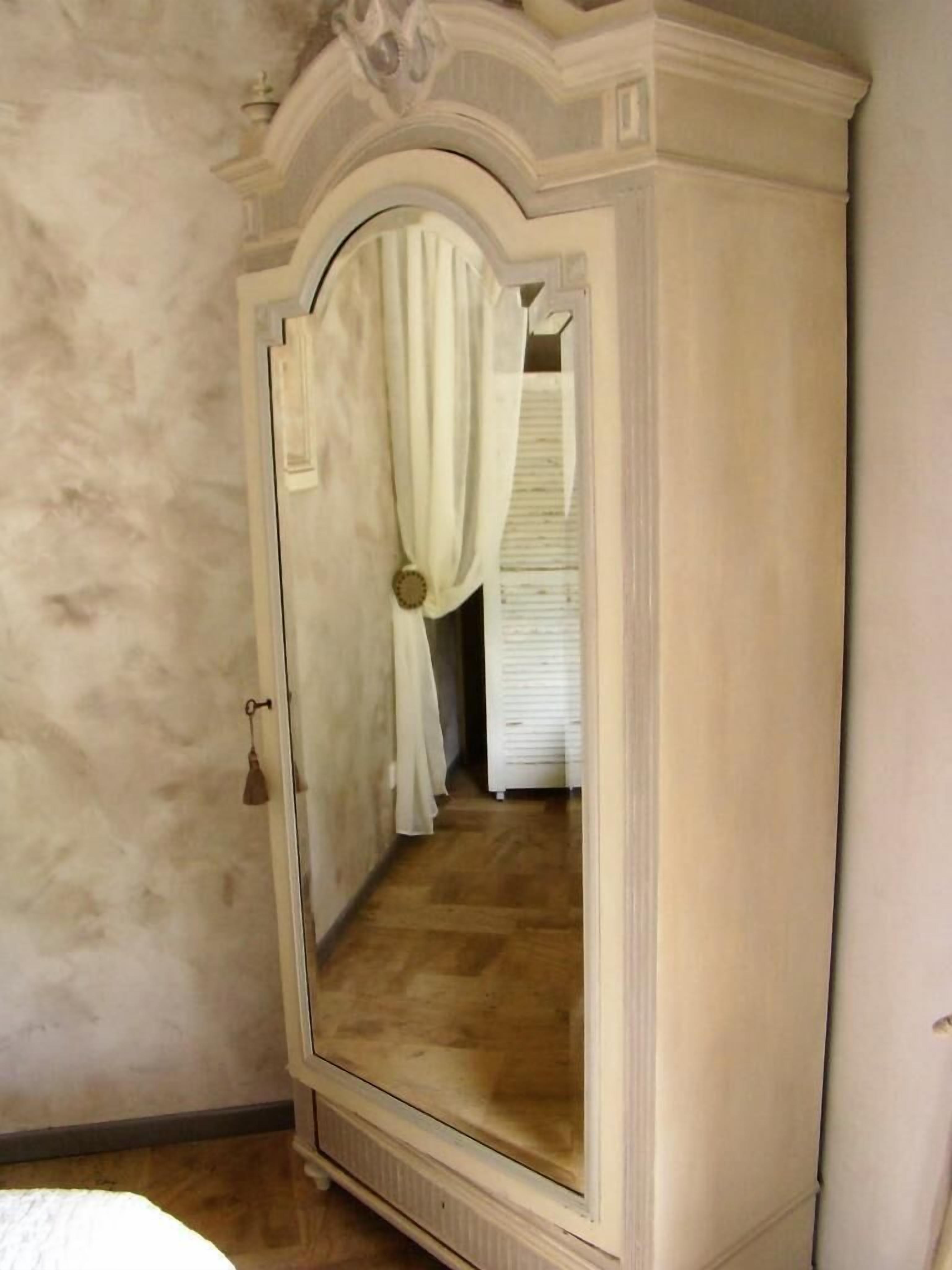 Una habitación con un espejo grande, piso de madera y una puerta blanca con cortina.