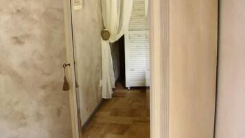 Una habitación con un espejo grande, piso de madera y una puerta blanca con cortina.