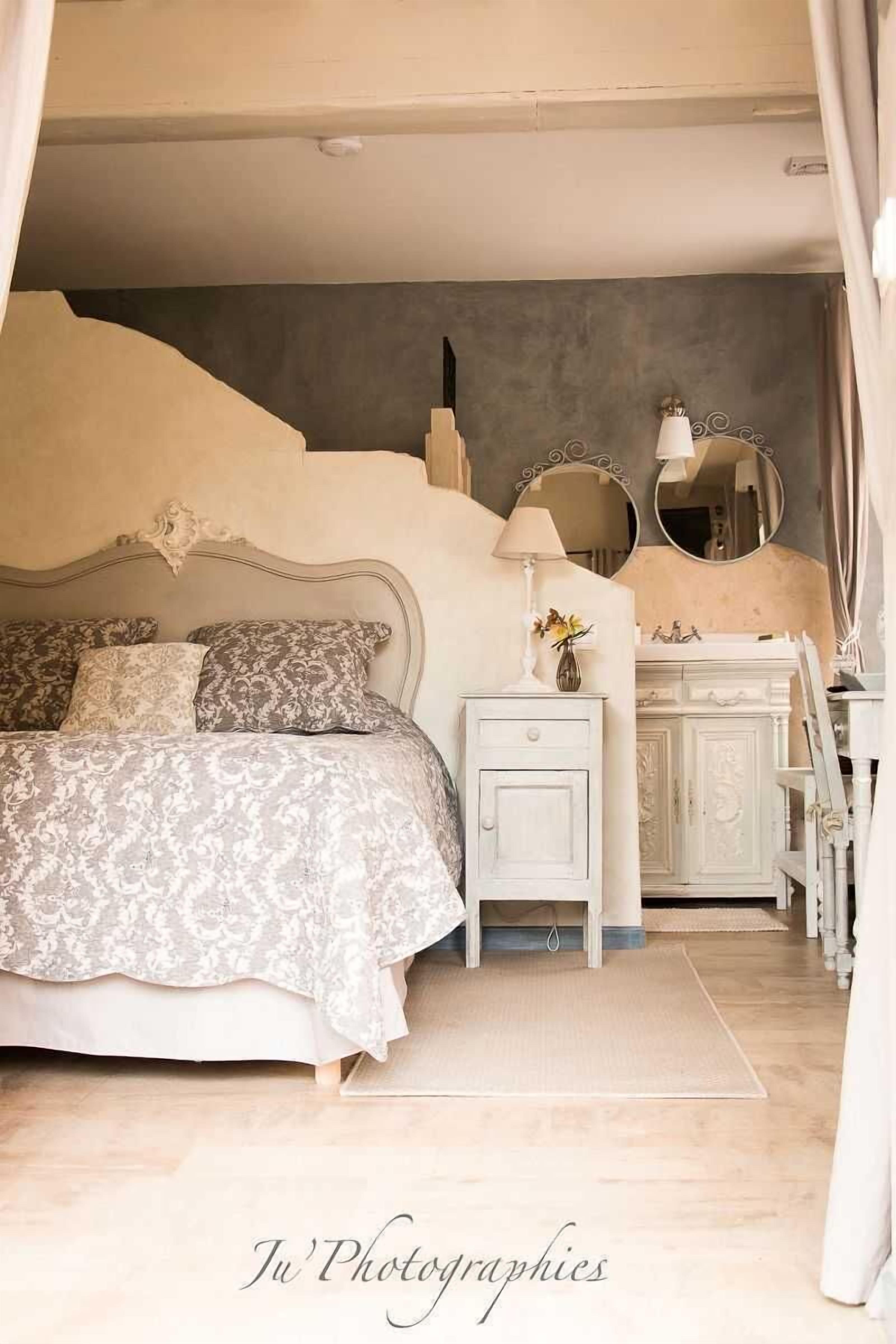 Un dormitorio con cama, mesita de noche, cómoda y dos espejos.