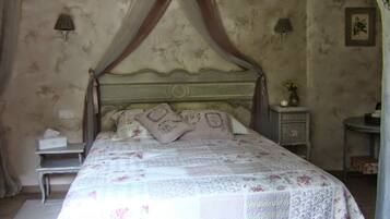 A bedroom with a four-poster bed, a nightstand, a bedside table, and a wall-mounted lamp.