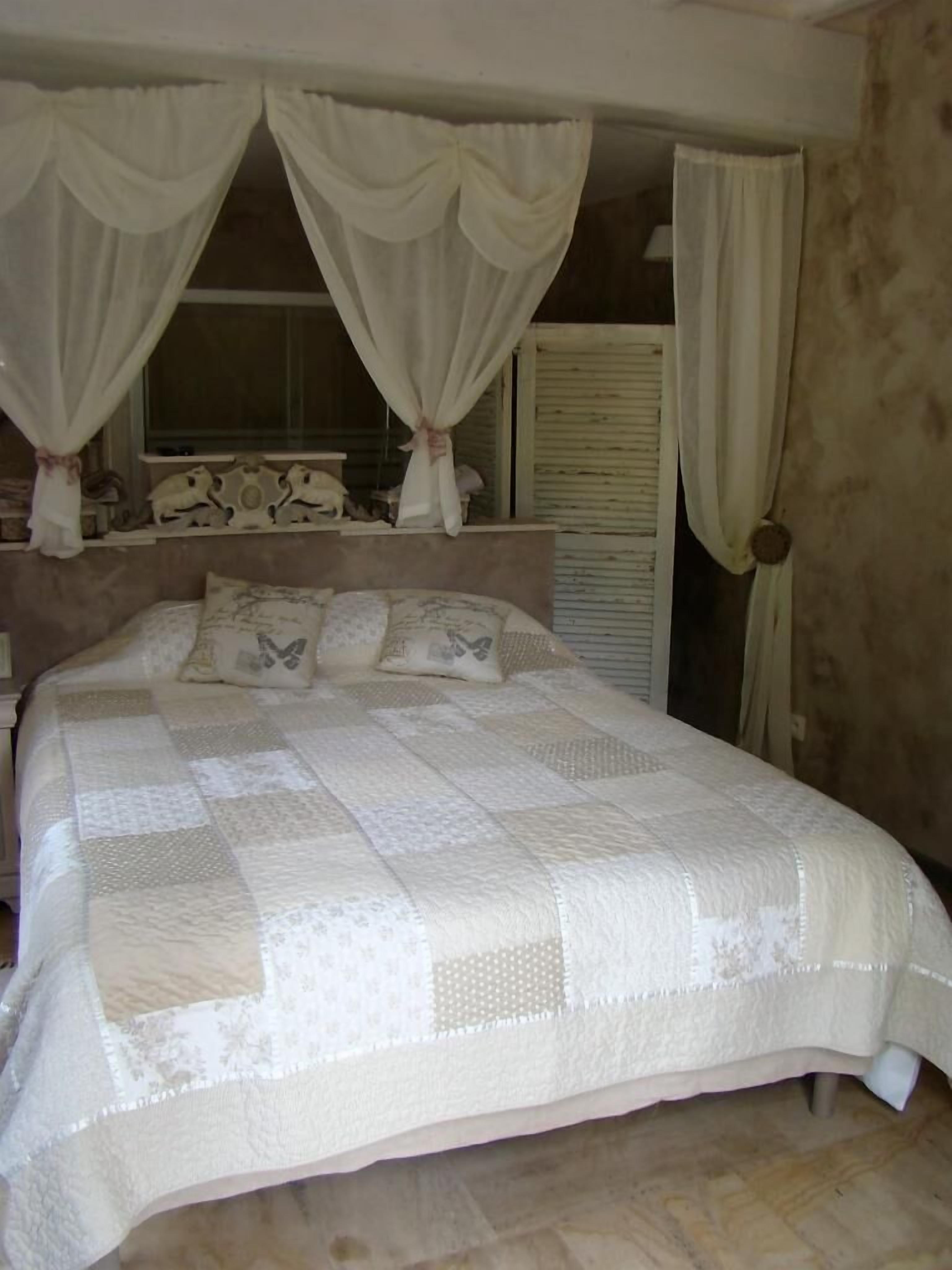 Une chambre à coucher avec un grand lit, des rideaux blancs et une fenêtre agrémentée de volets décoratifs.