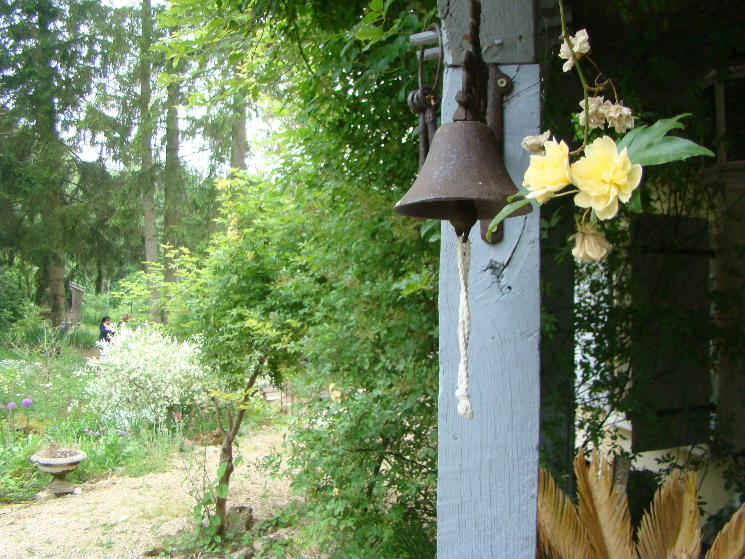 Un jardín con una campana en un poste de madera, rodeado de follaje y flores.