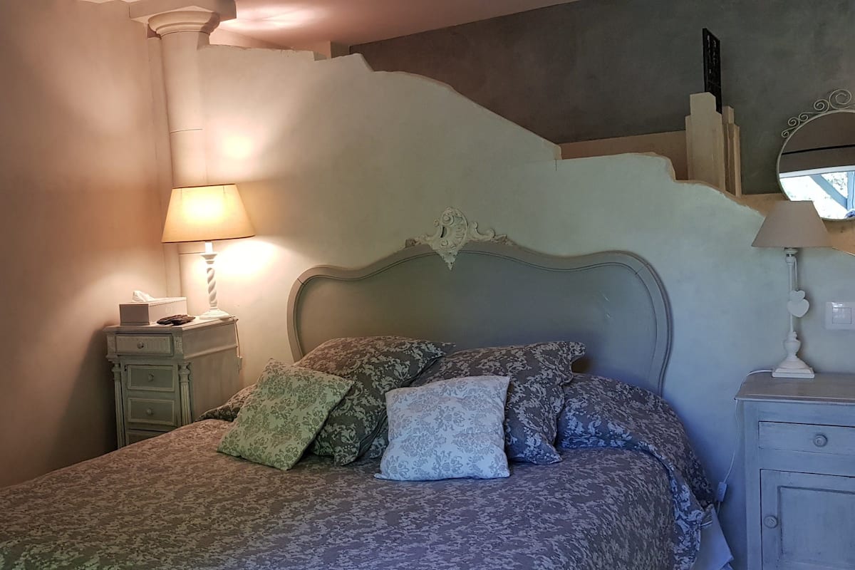 Une chambre à coucher avec un lit, deux tables de chevet, une lampe et un miroir.