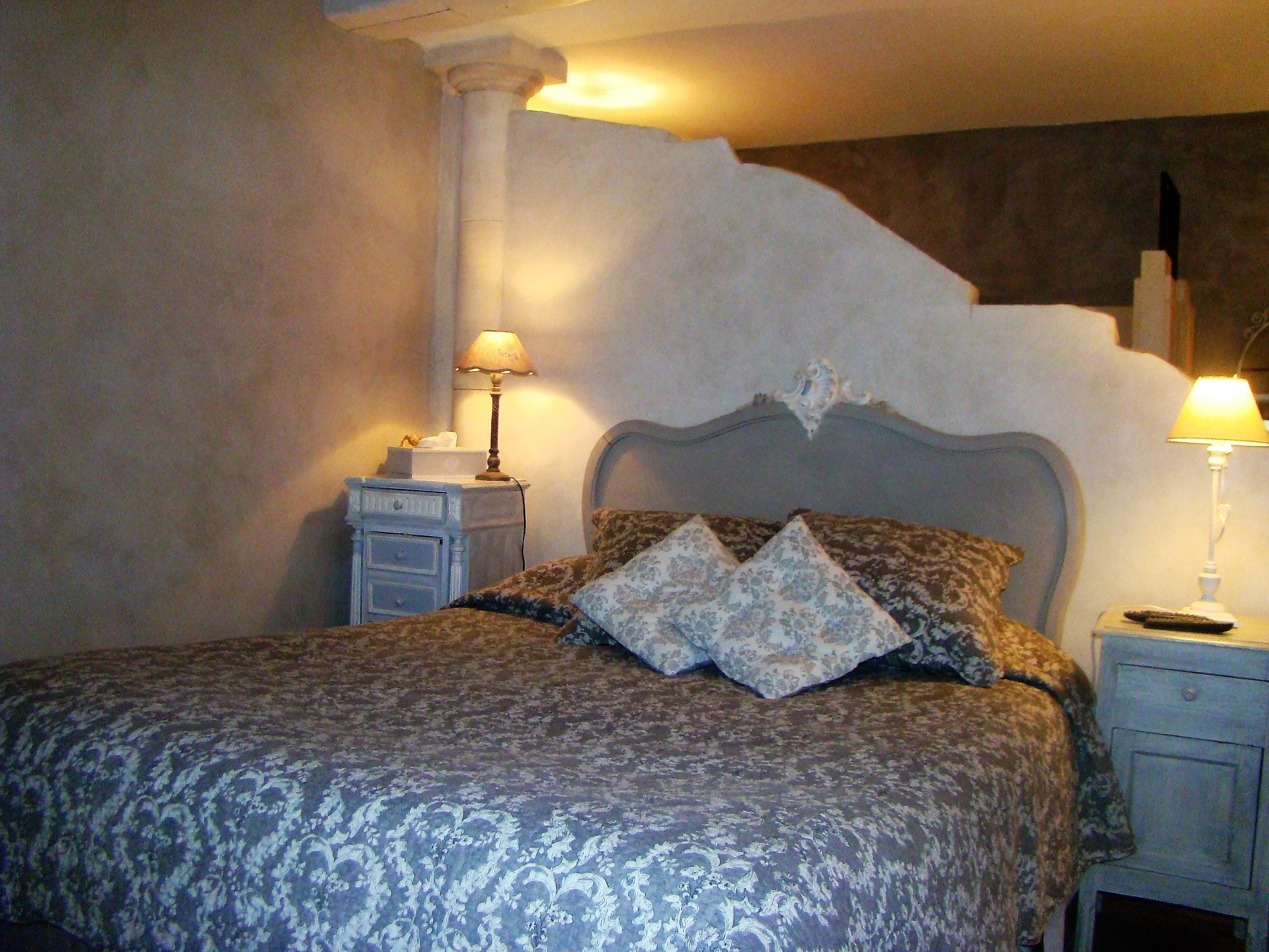 Un dormitorio con una cama, dos mesitas de noche, una lámpara sobre cada mesita y un edredón estampado.