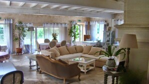 Un vaste espace de vie comprenant un grand canapé, une table basse et une table à manger avec des chaises. On y trouve également des plantes en pot et une lampe sur une table d’appoint.