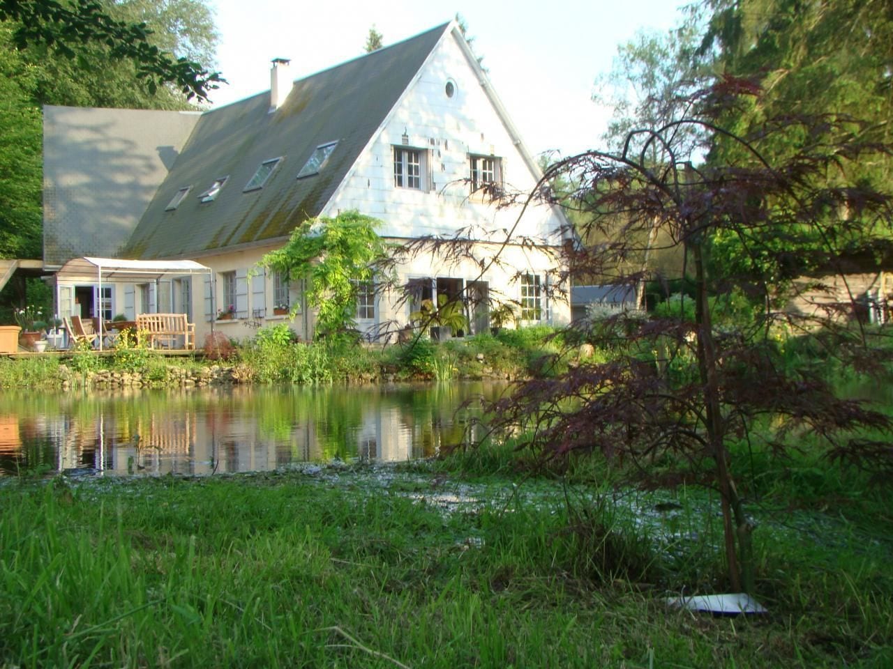Une maison avec un étang devant, une véranda et un toit en pente.