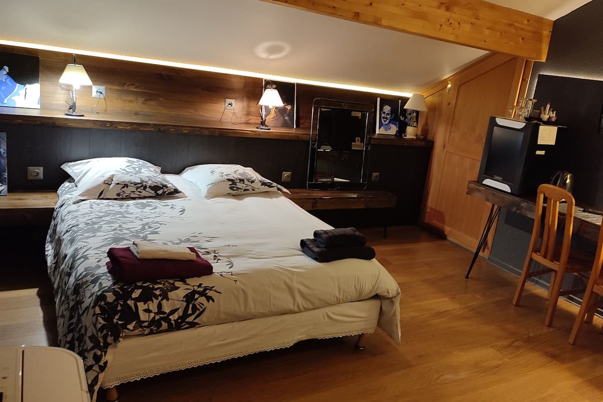 Een slaapkamer met een bed, nachtkastje, lamp en een bureau met stoel.