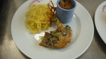 Een bord met een stukje kip, fettuccine en een klein blauw kopje saus.