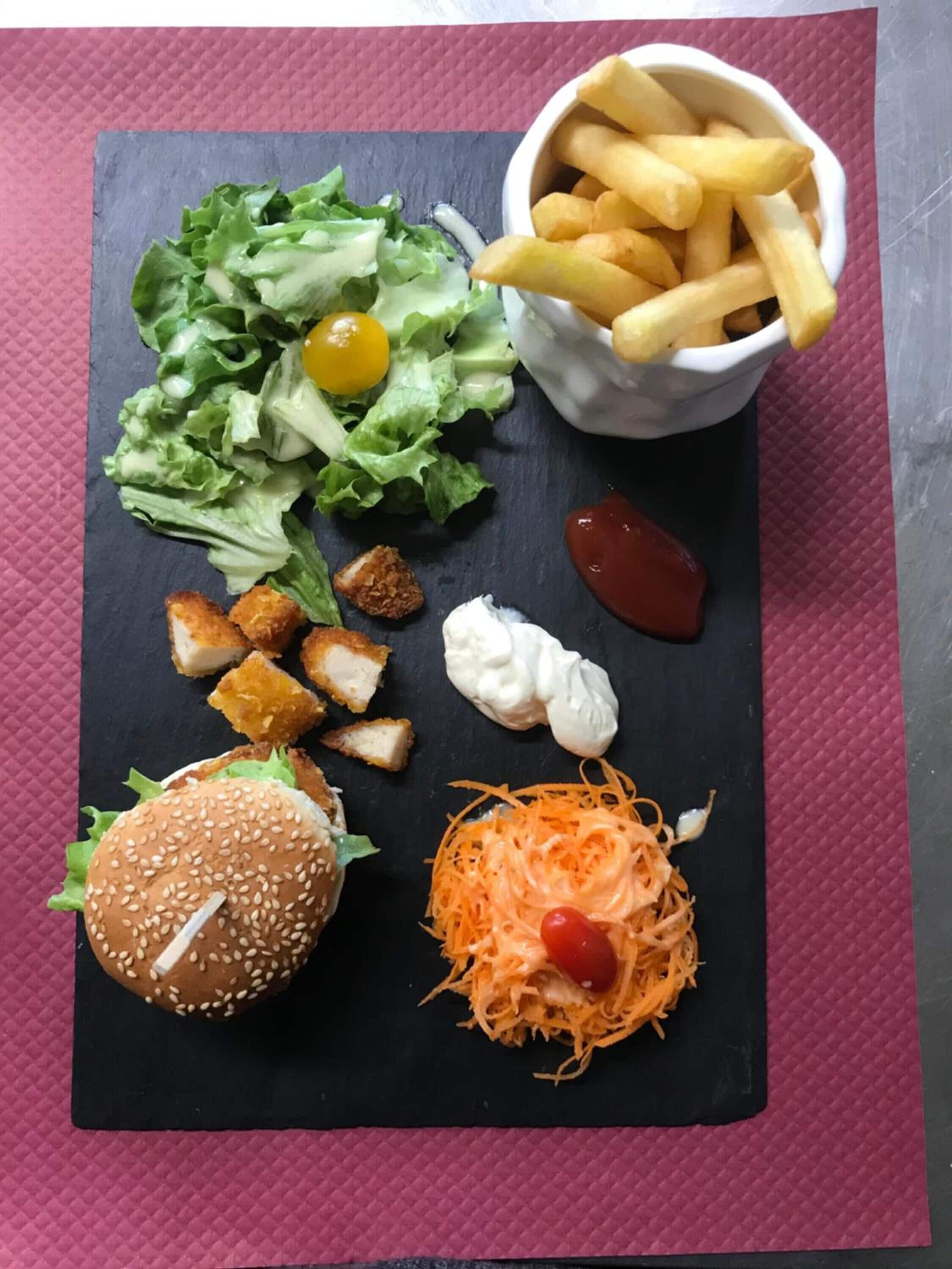 Uma refeição com hambúrguer, batatas fritas, salada e um pequeno pote de ketchup.