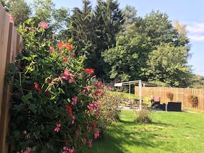 Un patio trasero con cerca de madera, un pérgola y diversas plantas y flores.