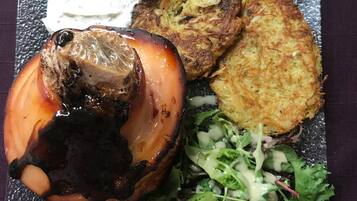 A plate with a grilled onion, two potato pancakes, a dollop of white sauce, and a side of greens.