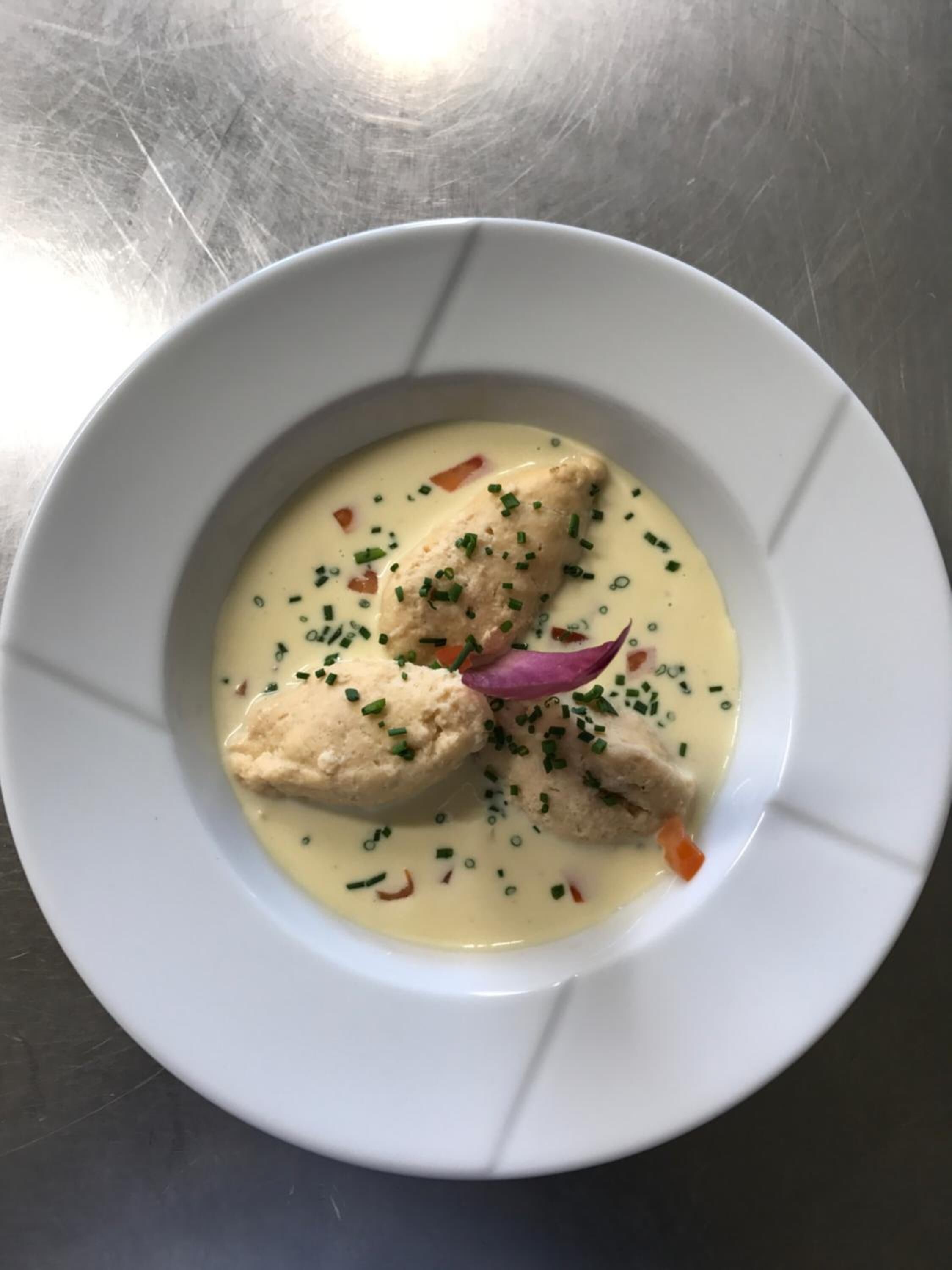 Un plato blanco con una crema, adornado con cebollino y cebolla morada.