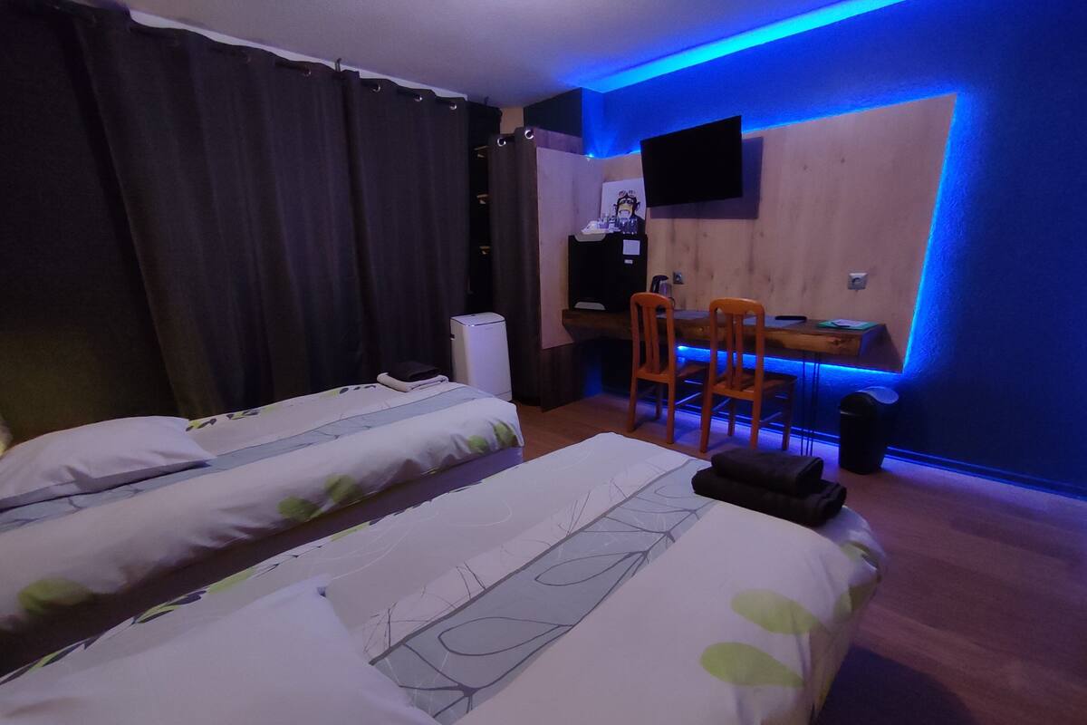 Een hotelkamer met twee bedden, een bureau, een stoel en een aan de muur bevestigde televisie.