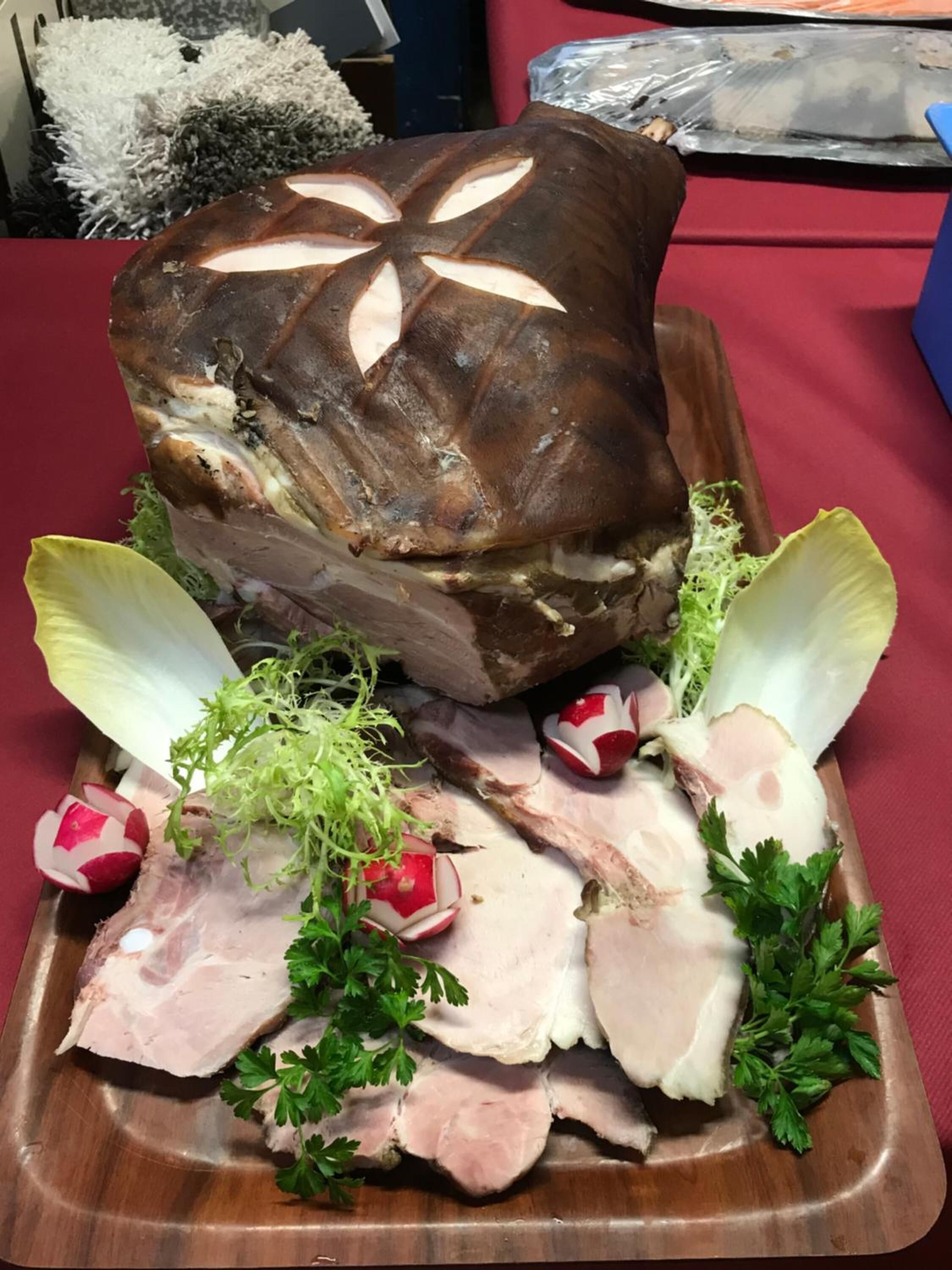 Un grand cochon rôti, présenté sur un plat en bois, accompagné de tranches de viande, de radis et de persil.