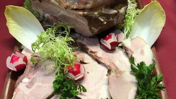 Un grand cochon rôti, présenté sur un plat en bois, accompagné de tranches de viande, de radis et de persil.