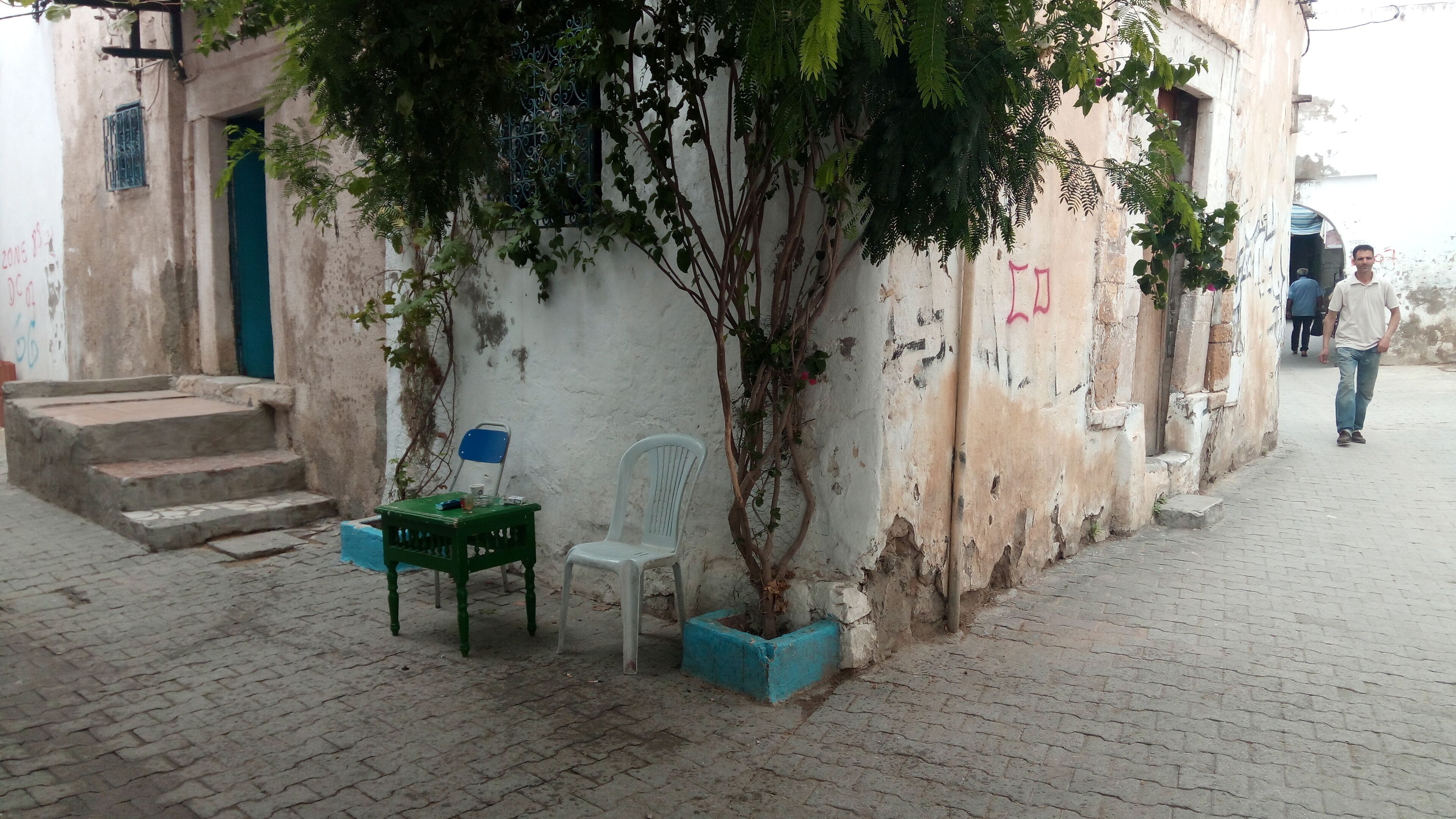 A narrow street with a building featuring a staircase and a tree growing against the wall.