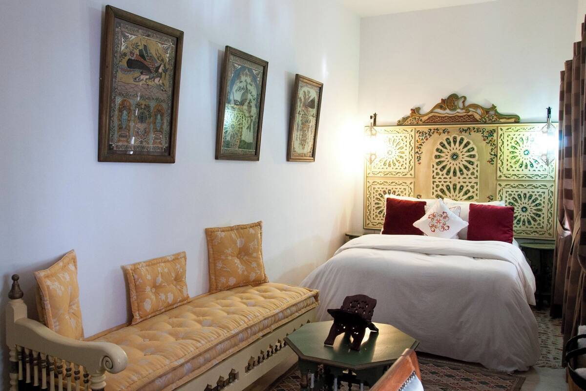 A room with a bed, a sofa, and three framed pictures on the wall.