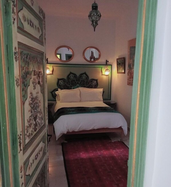 Un pasillo estrecho que conduce a un dormitorio con una cama, dos espejos en la pared y un cabecero decorativo.