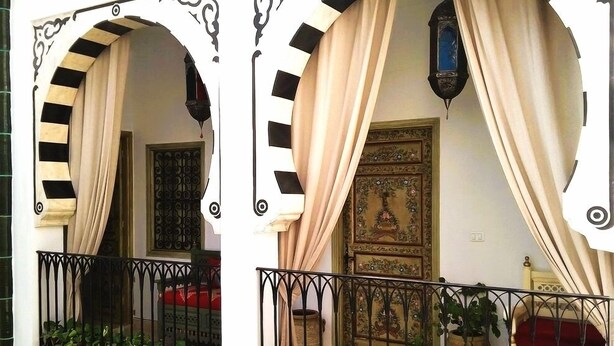 A balcony with a wrought iron railing, potted plants, and a traditional wooden door with intricate carvings. - El Patio Courtyard House (Tunis)