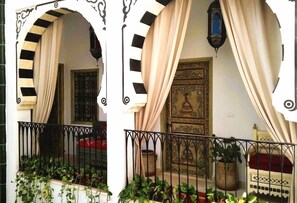 Un balcón con barandilla de hierro forjado, macetas con plantas y una puerta de madera tradicional con detalles tallados.