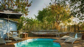Un área de piscina con sillones de descanso, una terraza de madera y una valla de bambú.