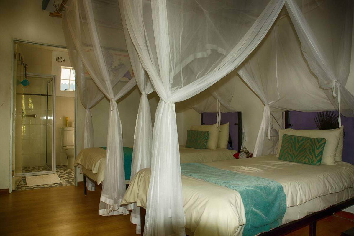 A room with a bed under a canopy, a shower area, and a nightstand with a lamp.