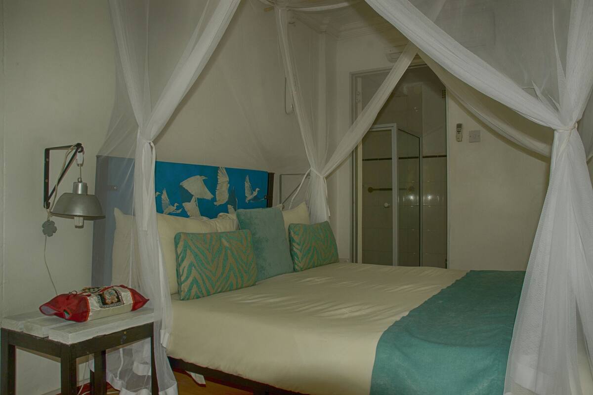 A bedroom with a bed, a nightstand, a lamp, a painting, and a door.