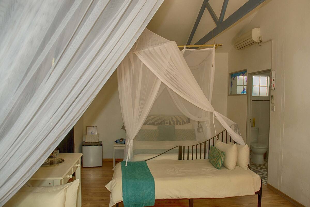 A bedroom with a four-poster bed, a bedside table, a nightstand, a small desk, and a chair.