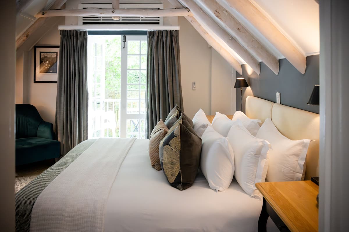 A bedroom with a large bed, a bedside table, a lamp, a chair, and a window with curtains.