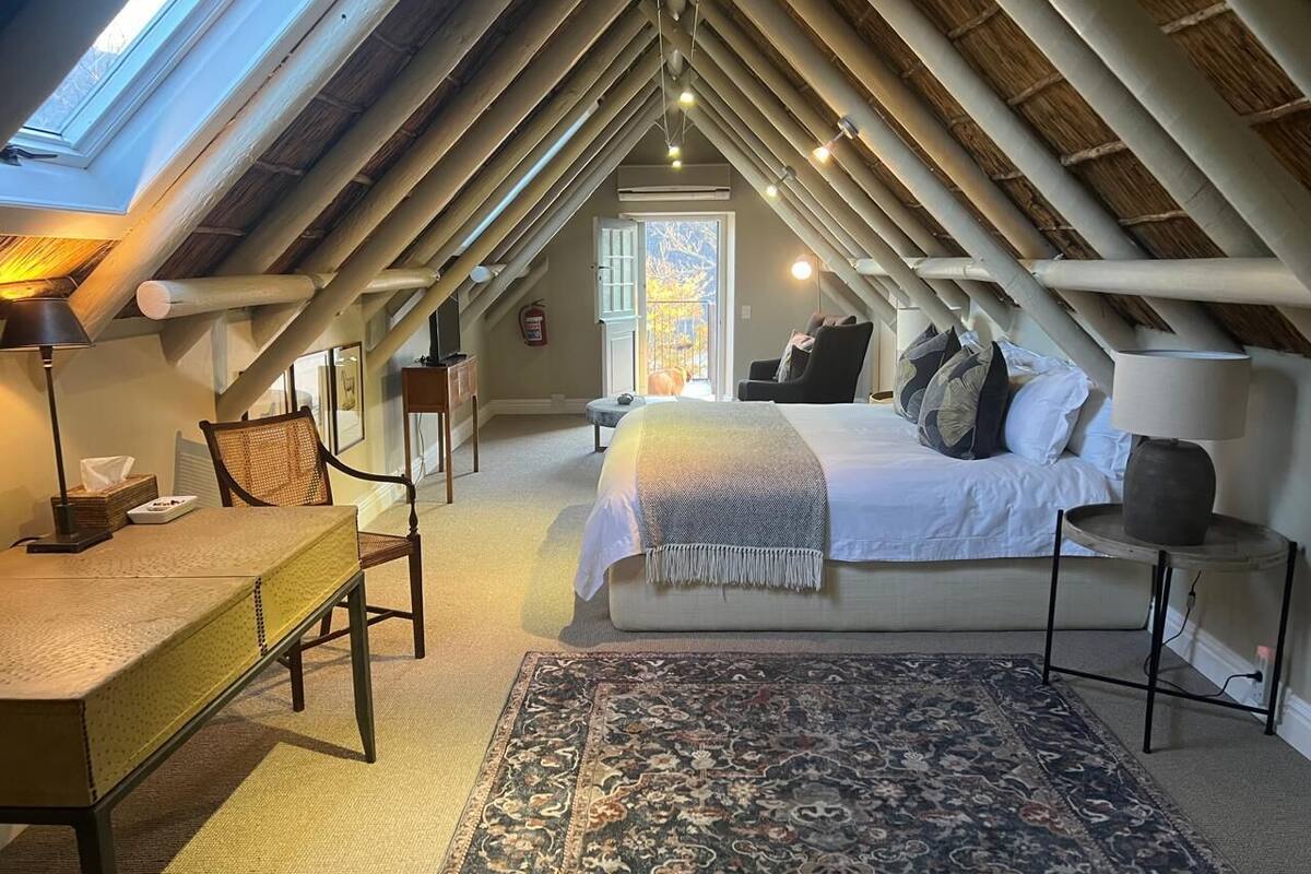 An attic bedroom with a sloped ceiling, a bed with white linens, a patterned rug, a wooden desk, and a chair.