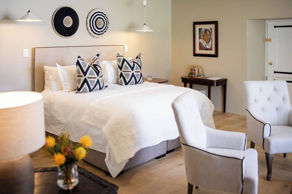 A neatly arranged bedroom with a large bed, a bedside table, a chair, and a small table with a lamp and flowers.