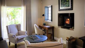 Una sala de estar acogedora con chimenea, un sillón cómodo, una mesita con lámpara y vistas al exterior con vegetación.